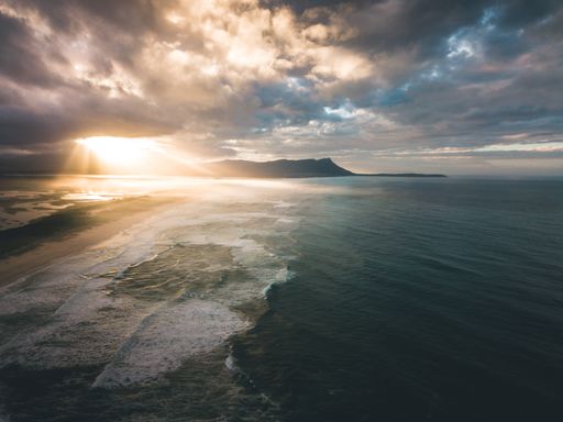 A breathtaking aerial view of a serene sea with gentle tides nearing the shore under the golden sun rays in a cloudy sky