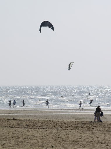 A vertical shot of kite surfers and people at the beach of Katwijk