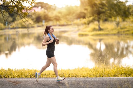 A scenic view of an athletic woman jogging by a lake on a beautiful day