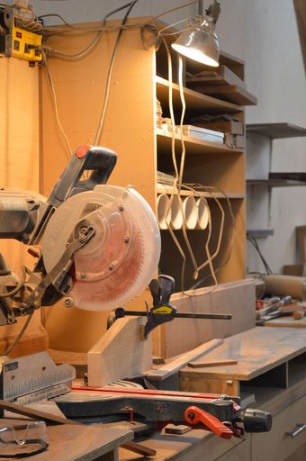 A vertical shot of a circular saw blade ready to cut wooden planks in a workshop with lamps pointing at it