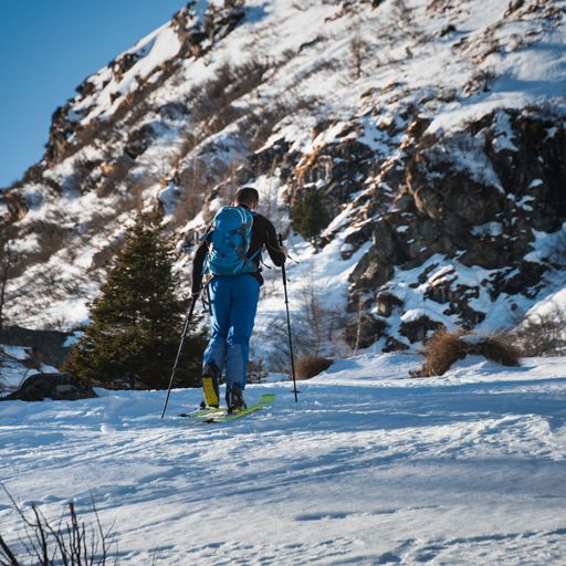 A man with a blue backpack skiing in the winter with a huge white mountain looming over him