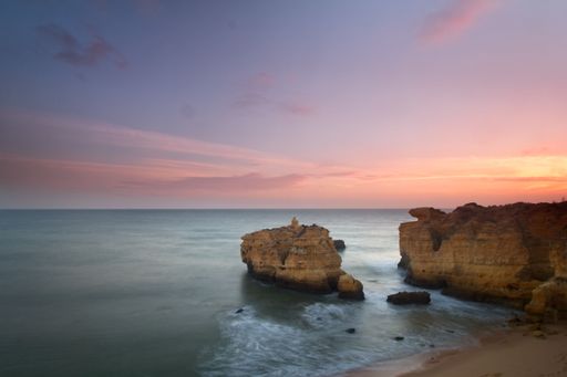 An aerial view of high cliffs in the blue ocean at mesmerizing colorful sunset, Algarve, Portugal