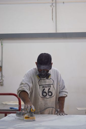 A vertical shot of a man in a protective mask using a woodworking sander in a workshop