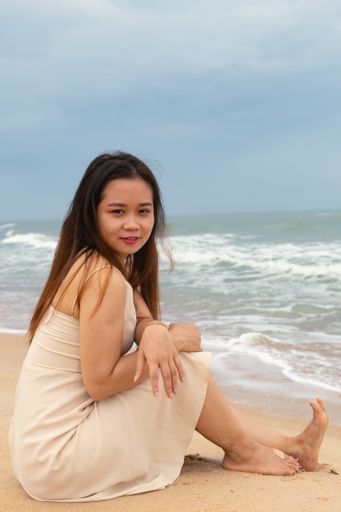 A vertical closeup shot of a young beautiful Asian female sitting and posing at the beach