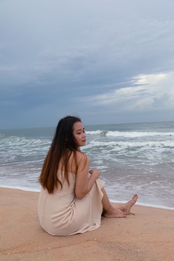 A beautiful Asian woman sitting on the sand near the beach and enjoying the calming wave sounds