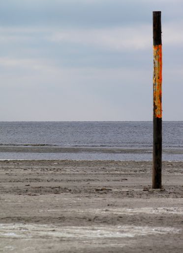 A vertical shot of wooden pole in front of a calm sea