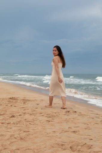 A beautiful Asian woman walking on the sand across the water and enjoying the calming wave sounds