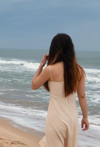 A beautiful Asian woman walking on the sand across the water and enjoying the calming wave sounds