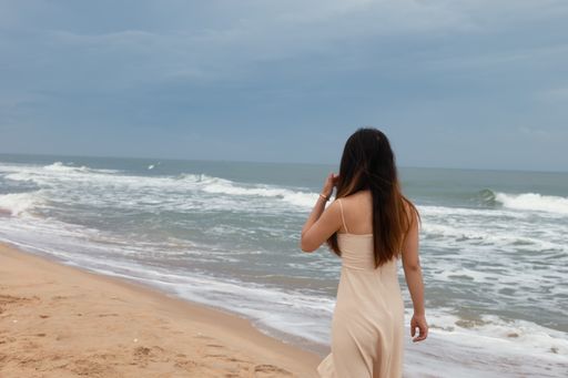 A beautiful Asian woman walking on the sand across the water and enjoying the calming wave sounds