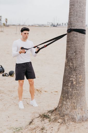 A young fit Spanish athletic male doing shoulder pull exercises with a rope at the beach