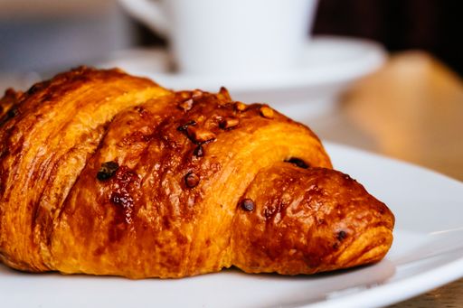 A selective focus shot of a croissant on a plate and a cup of coffee on a wooden surface