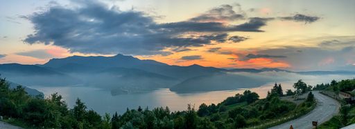A panoramic shot of an amazing shot of a road near a reflective lake on a sunset background