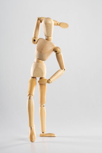 A vertical shot of a wooden pose doll with one hand behind its head and the other on its waist