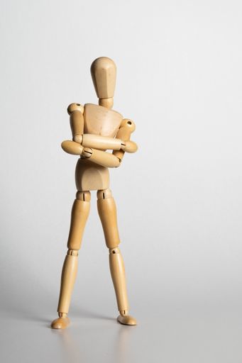 A vertical shot of a wooden pose doll with crossed arms standing on a white background