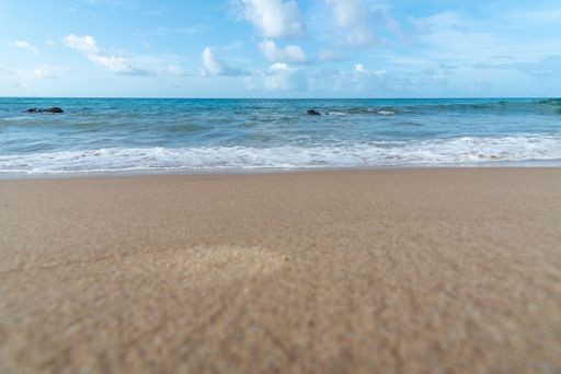 Low view of sandy beach with foamy waves against blue sky with clouds in the background. Barra beach, Salvador, Brazil.
