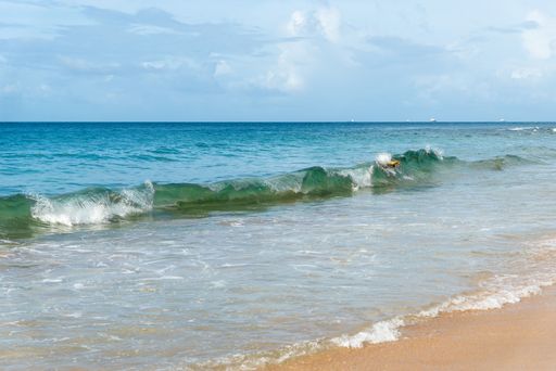 Low view of sandy beach with foamy waves against blue sky with clouds in the background. Barra beach, Salvador, Brazil.