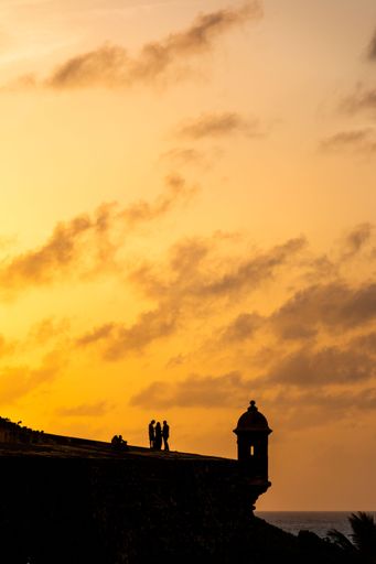 Vertical shot of silhouettes of people near the walls of El Morro Fort at golden sunset, old San Juan, Puerto Rico