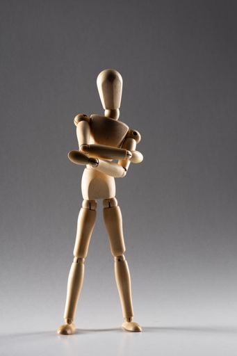 A vertical shot of a wooden pose doll with crossed arms standing in the shade on a white background