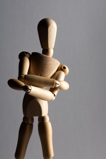 A vertical closeup shot of a wooden pose doll with crossed arms standing in the shade