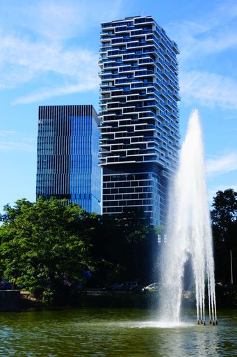 One Forty West Tower seen from Ludwig-Erhard-Anlage, Frankfurt, Germany. Senckenberg Tower in the background. Blue sky and water fountain.