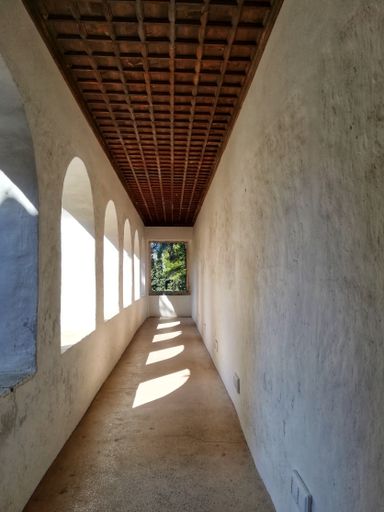 A vertical shot of a  long stone balcony with structural shadows falling from an arch-shaped stone windows
