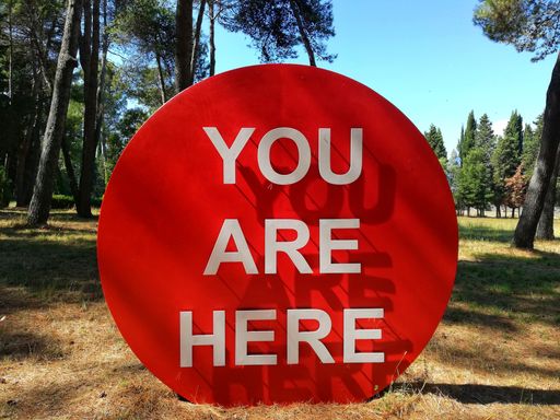 A red circle sign You Are Here  placed on a forested area