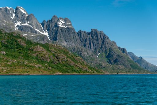 The Rulten mountain peak on the sea shore against blue sky in Norway