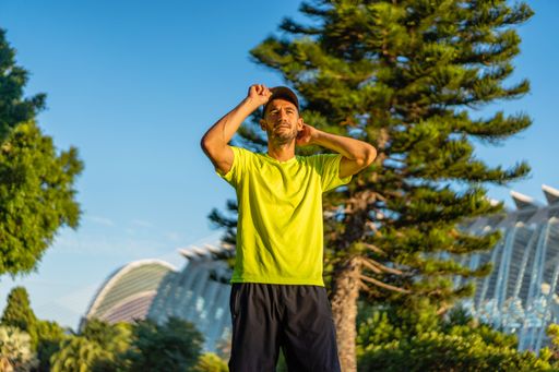 Low shot of hispanic man holding his cap in the park with modern buildings of the city of arts and sciences of Valencia in the background at sunset.