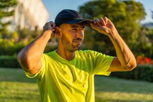 Portrait of hispanic man holding his cap in the park with modern buildings of the city of arts and sciences of Valencia in the background at sunset.