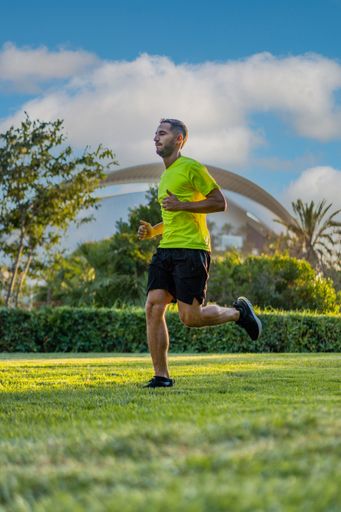 Hispanic handsome man wearing a yellow t-shirt jogging during sunset in the park garden of the city of arts and sciences, Valencia, Spain.