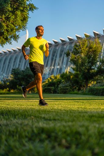 Hispanic handsome man wearing a yellow t-shirt jogging during sunset in the park garden of the city of arts and sciences, Valencia, Spain.