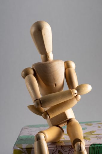 A vertical closeup shot of a wooden pose doll with crossed arms sitting on a floral box