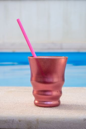 A vertical shot of colored glass with a straw near swimming pool
