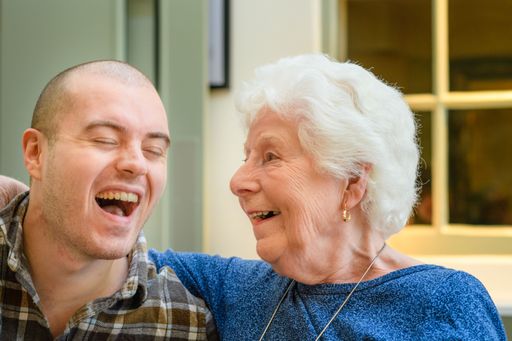 Two Caucasian people, a young male and an elderly woman laughing with each other