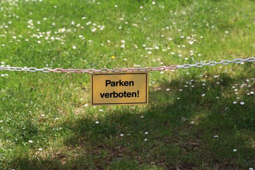 A closeup of a "No parking" sign  in German against a green lawn with flowers