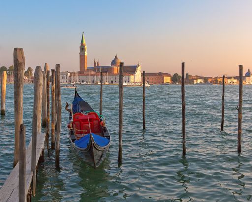 A boat and wooden poles in blue waters and cultural buildings in distance in Venice