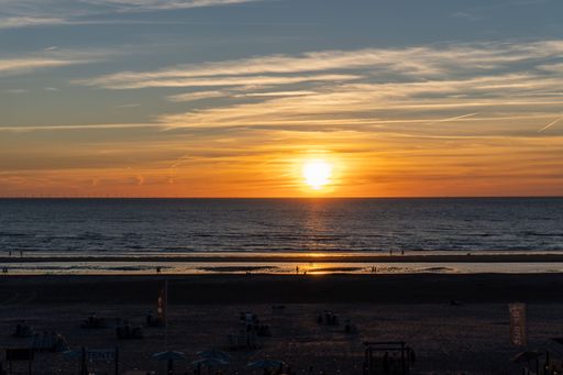 A bright golden sunset over the calm blue sea and the sandy beach with the horizon in the background