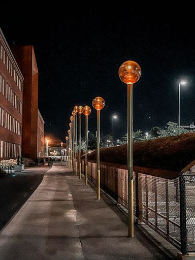 A vertical shot of orange globe street lamps along a walkway at night