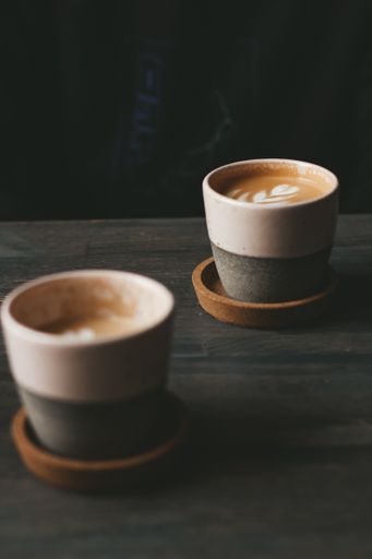 A vertical shot of two ceramic cups of foamy caffe latte on a wooden table