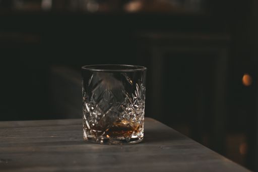 A closeup of an alcoholic drink in a crystal glass on a wooden table - alcoholism concept
