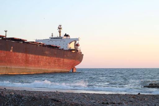 A cargo ship on the coast of an ocean with waves and a beautiful sunset in the background