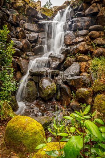 A vertical shot of a waterfall coming down the moss covered stones