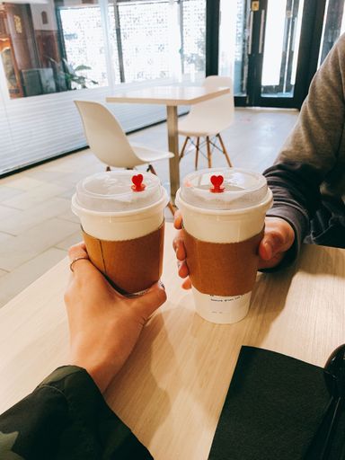A vertical closeup shot of hands holding cups of takeaway coffee