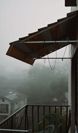 A vertical shot of an apartment balcony on a foggy day with a blurry neighborhood in the background