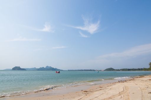 A sandy coast and a single boat in the middle of a tranquil sea before mountains and cliffs