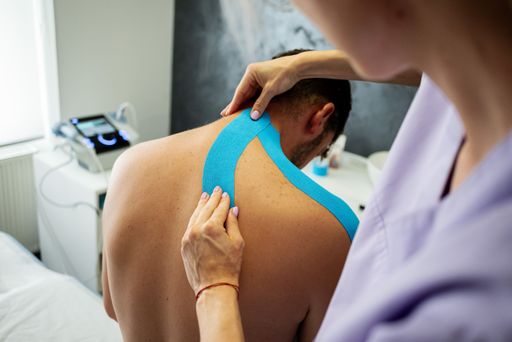 A physiotherapist applying tape on the neck and shoulders of a male patient during kinesiotherapy