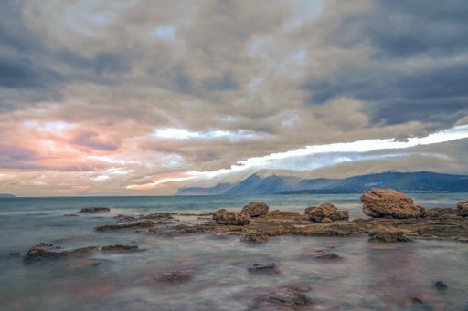A beautiful shot of the sea with rocks in the water and mountains the distance under a cloudy sky - great for a background