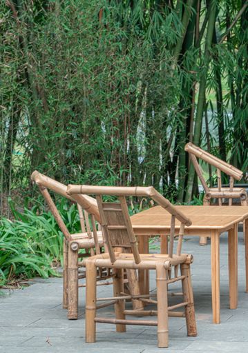 A vertical shot of wooden chairs and tables in a seat area next to the trees in a park