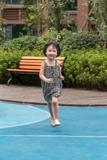 A vertical shot of a running girl in a kid's playing garden
