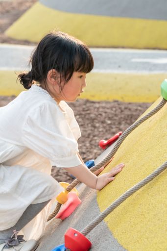 A vertical shot of a cute young Asian girl playing outdoors under the sun in a playground